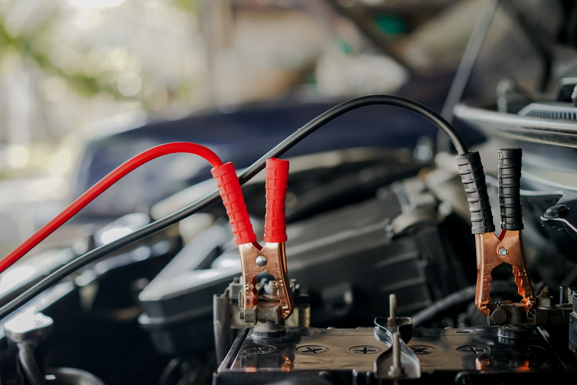 a dead car battery being started with jumper cables